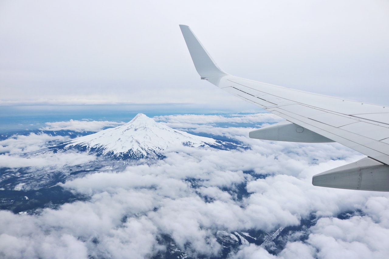 The view of a businessperson using an AI Model Business Intelligence Reporting software, from the wing of an airplane looking over a mountain covered in clouds